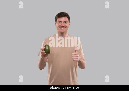 Mann hält Avocado und Daumen nach oben isoliert. Gesundes Leben, Essen Green Konzept Stockfoto