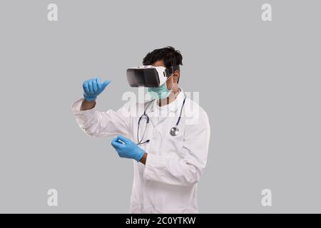 Arzt trägt VR-Brille, medizinische Maske und Handschuhe Hände in Front isoliert. Indian man Doctor Holding in Virtual Reality Stockfoto