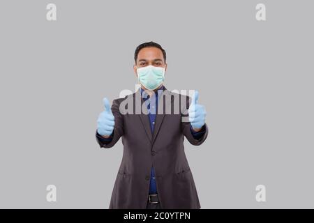 Geschäftsmann zeigt Schlag auf beide Hände tragen medizinische Maske und Handschuhe isoliert. Indian Business man stehend Thump up Zeichen Stockfoto