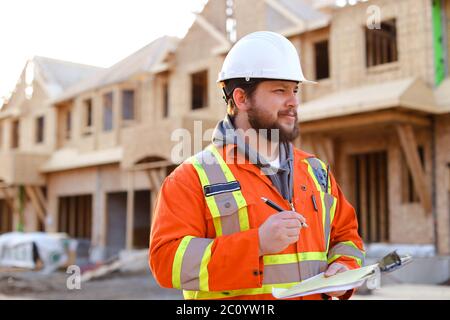 Kaukasischer Vorarbeiter schriftlich in Notebook auf der Baustelle. Stockfoto