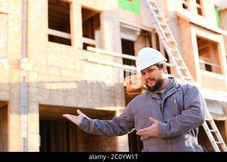 Portrait des kaukasischen Baumeisters, der fertige Gebäude zeigt und Hardhat trägt. Stockfoto