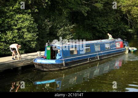 Zwei Männer, die ein blaues schmales Boot auf einem Steg auf dem Fluss Medway in der Nähe von Hadlow, Kent, anlegen Stockfoto