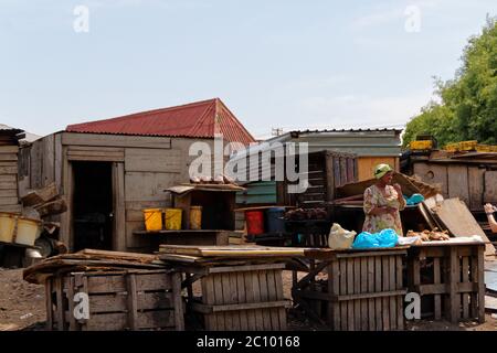 Kapstadt, Südafrika - Dez 4,2015: Frau vor Metzgerei und Haus mit Wellblechdach, Township. Sonniger Tag Stockfoto