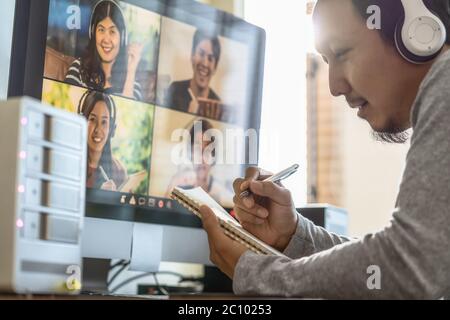 Nahaufnahme Asiatische Mann Hand Schreibbuch beim Online-Lernen über Videokonferenz mit Kollegen und Team Building Treffen, wenn Covid-19 Pandemie, Coro Stockfoto