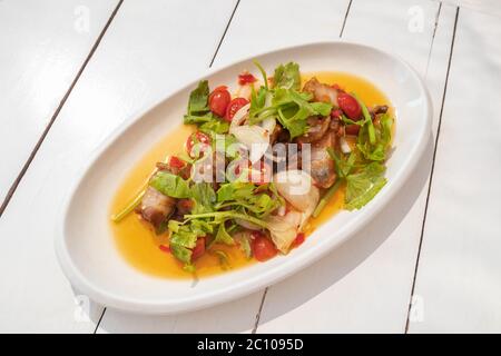 Knuspriger Schweinebauch würziger Salat auf weißem Teller und weißem Holztisch Stockfoto