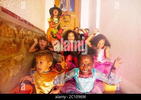 Viele vielfältig aussehende Kinder in Halloween Kostümen sitzen auf der Treppe der Tür des Hauses Stockfoto