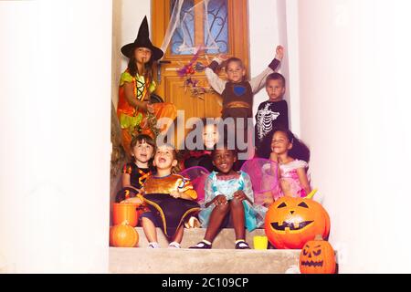 Halloween Gruppe von verschiedenen Kindern Portrait sitzen zusammen Jungen mit Mädchen auf der Treppe in der Nähe von Haus Tür halten Kürbis, Eimer schreien und lächeln Stockfoto