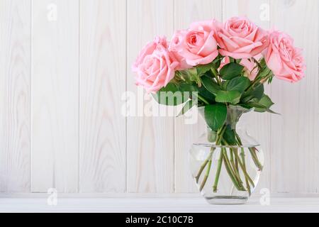 Blumenstrauß rosa Rosen in einer Glasvase auf einem hellen Holzbrett, floraler Hintergrund. Festlicher Rahmen, Geschenkkarte mit Kopierfläche, florales Layout Stockfoto