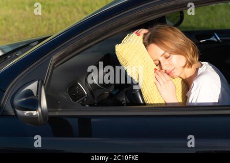 Müde junge Frau Fahrer schlafen auf Kissen auf Lenkrad, Ruhe nach langen Stunden mit dem Auto. Müdigkeit. Schlafentzug. Stockfoto