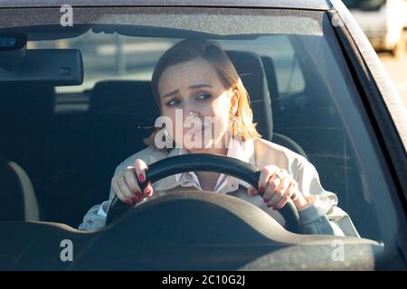 Frau fährt ihr Auto zum ersten Mal, versucht einen Autounfall zu vermeiden, ist sehr nervös und ängstlich, sorgt sich, klammert sich fest am Rad. Unerfahrenwerden Stockfoto