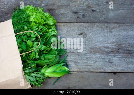 Frisches Gemüse in einem Papierbeutel - grüne Zwiebeln, Dill, Petersilie, Spinat, Rucola, Sauerampfer. Lieferung von Lebensmitteln und frischem Gemüse nach Hause. Holzhintergrund Stockfoto