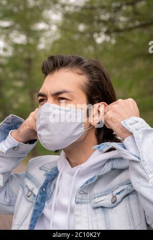 Brunette Mann in Denim Jacke im Freien stehen und setzen Stoffmaske auf Gesicht Stockfoto