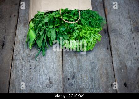 Frisches Gemüse in einem Papierbeutel - grüne Zwiebeln, Dill, Petersilie, Spinat, Rucola, Sauerampfer. Lieferung von Lebensmitteln und frischem Gemüse nach Hause. Holzhintergrund Stockfoto