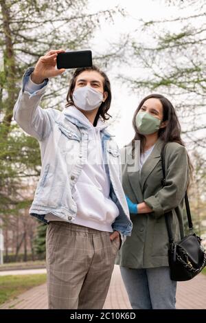 Mann mittleren Alters in lässigem Outfit stehen im Park und fotografieren mit Frau in Maske Stockfoto