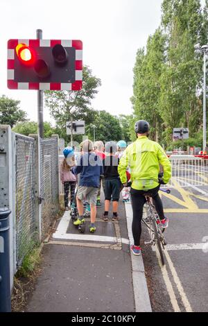 Ein Radfahrer und eine Gruppe kleiner Kinder warten am Bahnübergang Vine Road von Network Rail in Barnes, im Südwesten Londons, England, Großbritannien Stockfoto