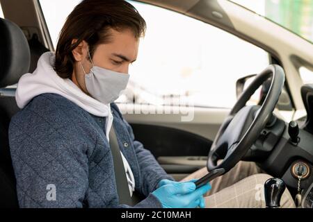Serious Brunette Taxifahrer in Stoffmaske sitzen am Lenkrad und Überprüfung der Karte Punkt auf dem Smartphone Stockfoto