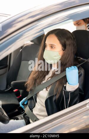 Taxifahrerin in Stoffmaske und Latexhandschuhen mit Sicherheitsgurt vor Taxifahrt während der Coronavirus-Pandemie Stockfoto