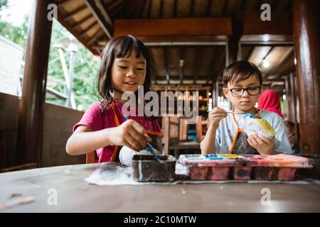 Kleines Mädchen und ein Junge machen Handwerk und Malerei Keramik-Objekt an einem Tisch Stockfoto