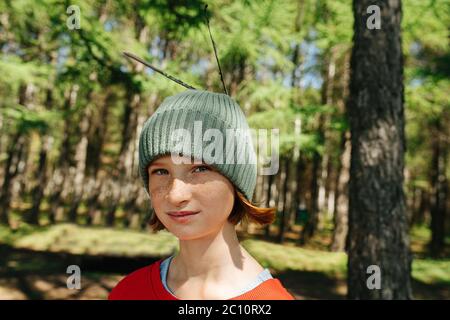 Porträt eines Sommersprossen-Mädchens in einem Wald mit Federn in der Mütze. Stockfoto