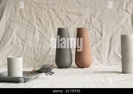 Stillleben Komposition aus zwei handgefertigten Tonvasen, weißen Keramikgläsern, grauem kleinen Tablett mit Bund von trockenem Lavendel gegen Leinentuch Stockfoto