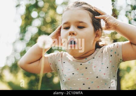 Nettes Kleinkind Mädchen Schläge auf Löwenzahn, Nahaufnahme Porträt am sonnigen Sommertag Stockfoto