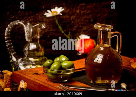 Natives Olivenöl extra, zuerst kalt gepresst, in einem Glas mit grünen Oliven auf einem rustikalen Hintergrund. Stockfoto