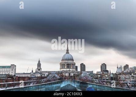 Die Menschenmassen von Einheimischen und Touristen überqueren die Themse in London über eine Fußgängerbrücke, wobei die Kuppel der St. Paul's Cathedral unter bedrohlichen Regenwolken steht. Lo Stockfoto