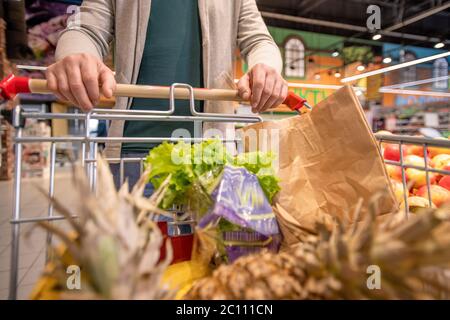 Hände von modernen reifen männlichen Kunden schieben Wagen mit frischem Obst und Gemüse, während Sie Supermarkt zu kaufen Lebensmittel Stockfoto