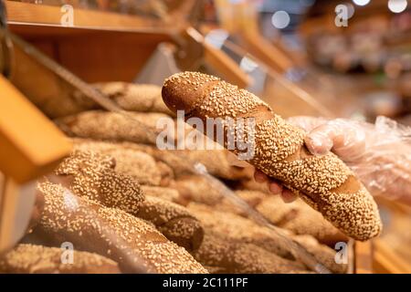 Handschuhen der reifen weiblichen Käufer hält frisches Brot mit Sesam bestreut, während im Supermarkt stehend Stockfoto