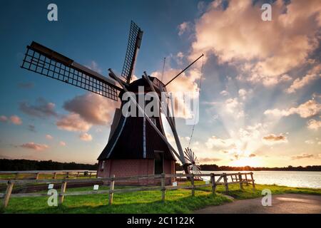 Charmante holländische Windmühle am See bei Sonnenuntergang Stockfoto