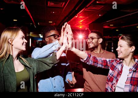 Zwei glückliche junge interkulturelle Paare in Casualwear geben einander High fünf nach dem Spiel der Bowling im Entertainment-Center Stockfoto