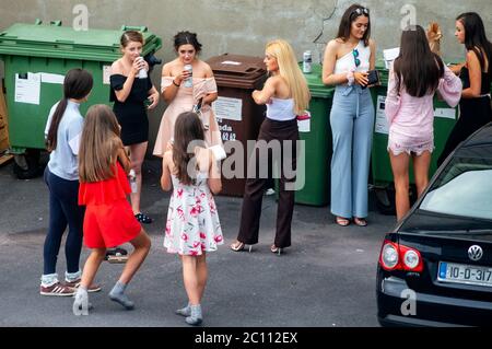 Junge Frauen und Teenager in eleganten Prom-Kleidern, die auf dem öffentlichen Parkplatz im Garten illegal alkoholisches Bier trinken, bevor sie als soziales Problem zu ihrer Abschlussfeier gehen. Stockfoto