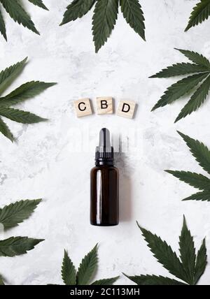 CBD-Öl in der Flasche um Cannabisblätter und in der Nähe von Holzbuchstaben CBN auf weißem Hintergrund flach legen. Stockfoto