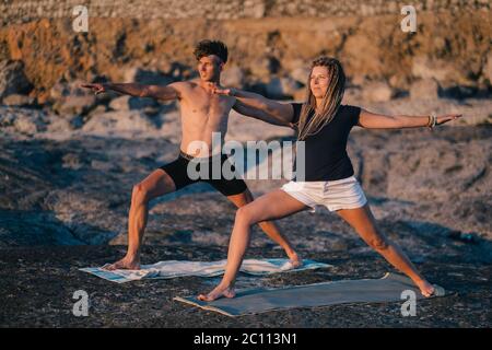 Paar, die Yoga bei Sonnenaufgang am Strand mit Blick auf das Meer praktizieren Stockfoto