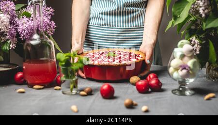 Kochen hausgemachte Cranberry Pie. Eine weibliche Konditorei hält eine fertige Preiselbeertarte mit weißer Sauerrahm. Tisch mit hellen Zutaten in Stockfoto