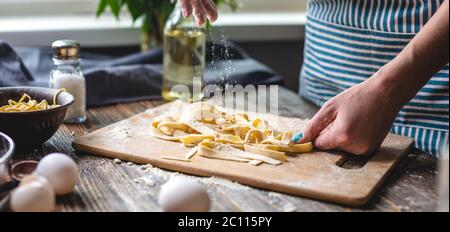 Frau ist sorgfältig bestreuen Mehl auf rohe frische hausgemachte Nudeln. Konzept des Prozesses der Zubereitung von handgemachten Pasta in einer gemütlichen Atmosphäre Stockfoto