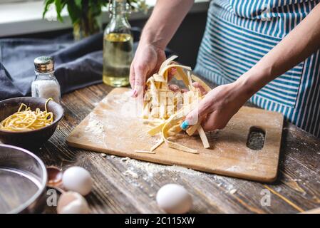 Frau hält sorgfältig frische, hausgemachte Nudeln in den Händen. Konzept des Prozesses der Zubereitung von handgemachten Pasta in einer gemütlichen Atmosphäre Stockfoto