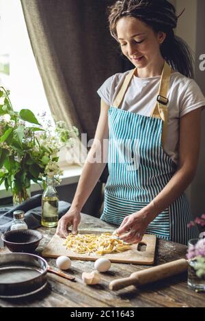 Frau hält sorgfältig frische, hausgemachte Nudeln in den Händen. Konzept des Prozesses der Zubereitung von handgemachten Pasta in einer gemütlichen Atmosphäre Stockfoto