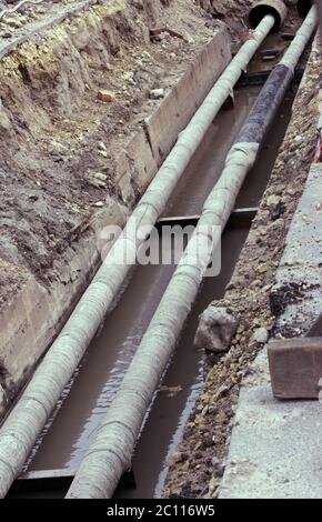 Wasserleitungen, isolierte Dachbleche während der Reparatur in einem Graben mit schlammigem Flüssigkeit gefüllt Stockfoto