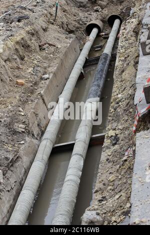 Wasserleitungen, isolierte Dachbleche während der Reparatur in einem Graben mit schlammigem Flüssigkeit gefüllt Stockfoto