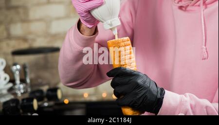 Barkeeper Zugabe von Sauce in französisch Hot Dog Roll Stockfoto