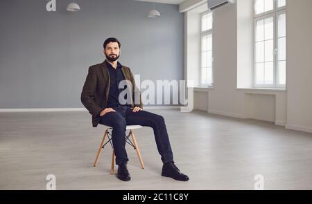 Eleganter junger Mann, der im leeren Raum sitzt Stockfoto