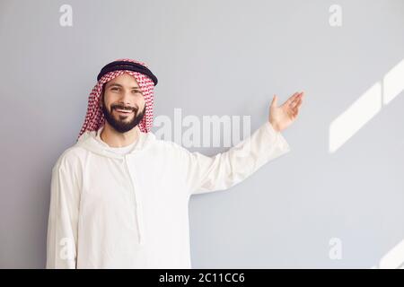 Der attraktive lächelnde arabische Mann zeigt seine Hand auf einen grauen Hintergrund Stockfoto