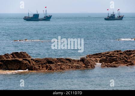 Zwei chinesische Fischerboote vor der Küste in der Fushan Bay bei Qingdao China in der Provinz Shandong an einem sonnigen, wolkenlosen Tag festgemacht. Stockfoto