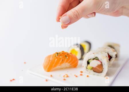 Weibliche Hand Spicing Lachs nigiri auf Sushi Set Teller isoliert auf weißem Hintergrund. Konzept für die Zubereitung japanischer Speisen. Stockfoto