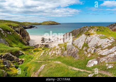 ACHMELVICH BAY UND STRAND SUTHERLAND HIGHLANDS SCHOTTLAND EIN BLAUER HIMMEL EIN TÜRKISFARBENES MEER UND EIN PFAD ZWISCHEN GELBEN BLUMEN VON VÖGELN FUSS TREFOIL LO Stockfoto