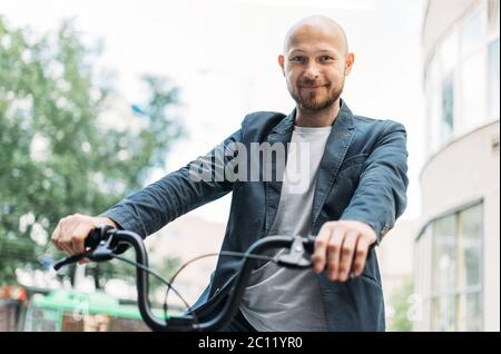 Erwachsener freundlicher Mann mit kahlem Bart in blauem Anzug auf dem Fahrrad in der Stadt Stockfoto