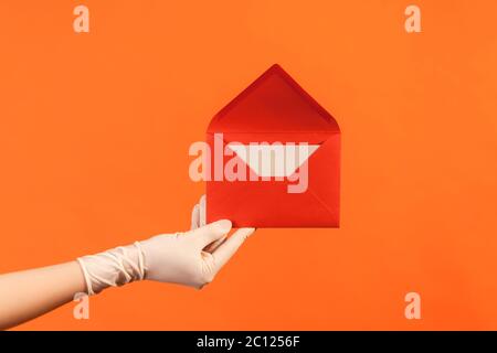 Profil Seitenansicht Nahaufnahme der menschlichen Hand in weißen OP-Handschuhen mit rot geöffneten Briefumschlag. Innen, Studio-Aufnahme, isoliert auf orangenen Rücken Stockfoto