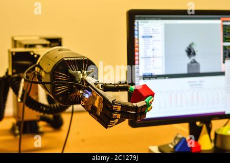 Roboterhand hält einen Red Cube im Forschungslabor. Unscharfer Computerbildschirm im Hintergrund. Stockfoto