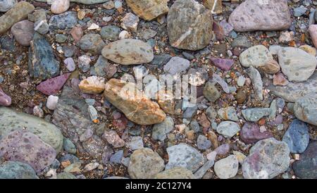 Struktureller Hintergrund aus Strandkieseln, Felsen und Sand entlang der Strandlinie eines geschützten kornischen Strandes. Stockfoto